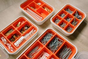 A set of orange plastic containers filled with screws and nails, including bolts and hex bolts.