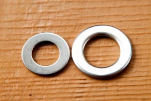 Two silver washers and a bolt on top of a wooden surface.