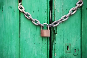 A padlock is secured to a green wooden door with nylon lock nuts.